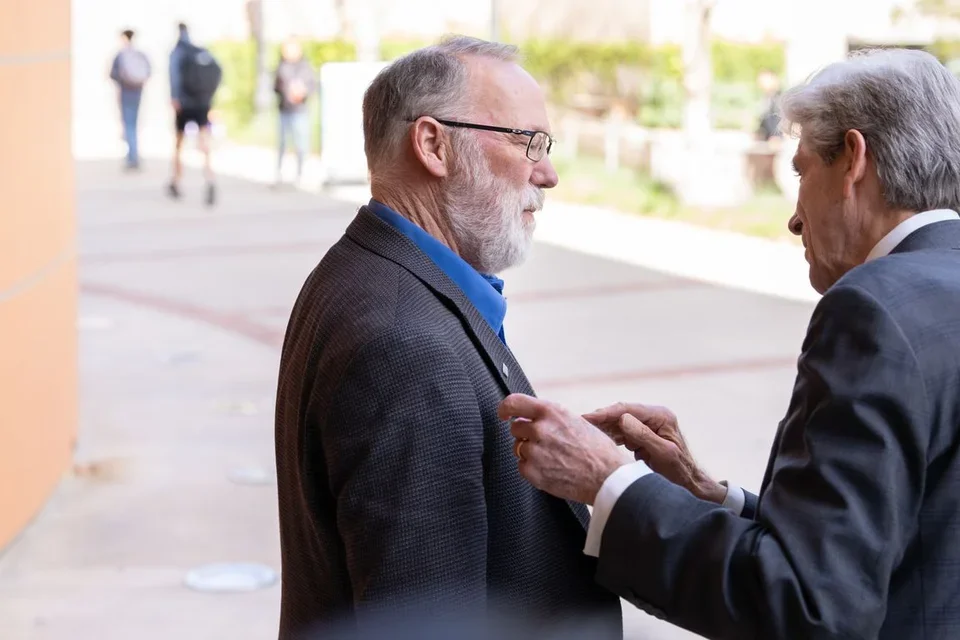 Chancellor Julio Frenk (right) removes a UCLA pin from his own suit jacket and fastens it onto Ramsdell’s lapel.